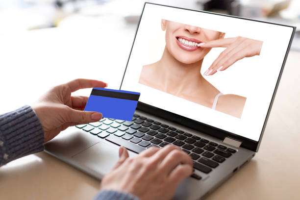 Payment for service via the internet. Female hands with credit card and open laptop with advertising of the dental industry in the screen, selective focus. Online shopping, personal data, contactless pay, customer, demand, supply concept.
