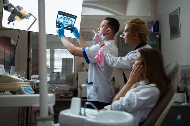 Young woman dentist and young man dentist holding and examining x-ray image with a female patient in the dentist's office