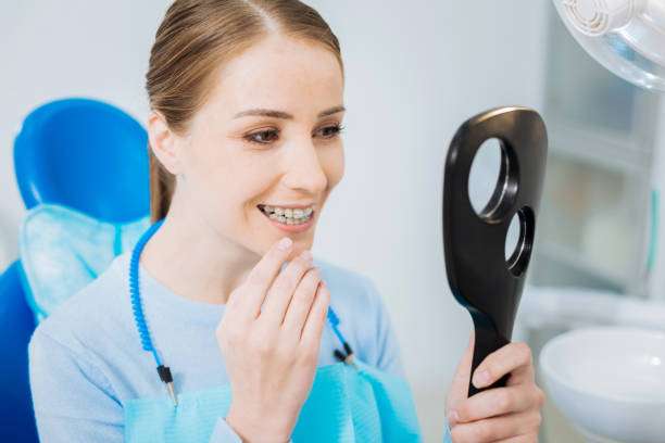 Beautiful smile. Delighted positive beautiful woman looking in the mirror and smiling while visiting a dentist