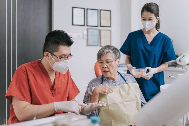 Asian Chinese male dentist explaining dental bridge on a tooth model to senior woman Patient