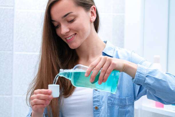 Happy smiling healthy young woman using in bathroom a mouthwash gel to rinsing mouth, fresh breath, dental and gums health. Oral hygiene and teeth care